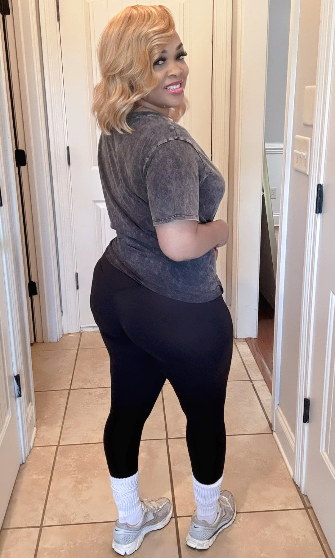 Rear view of model wearing washed black oversized top with black leggings, white socks, and silver sneakers indoors.