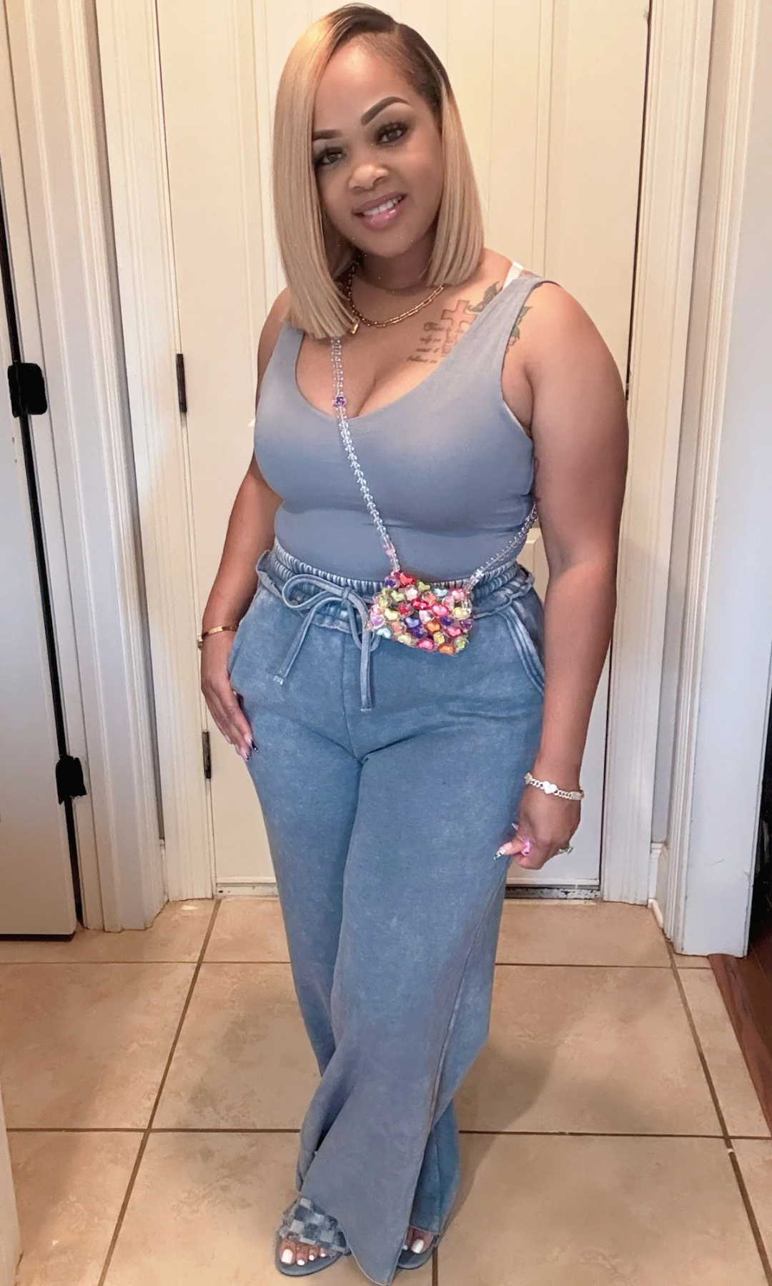 Model in teal tank top and wide-leg pants with colorful beaded crossbody bag indoors.