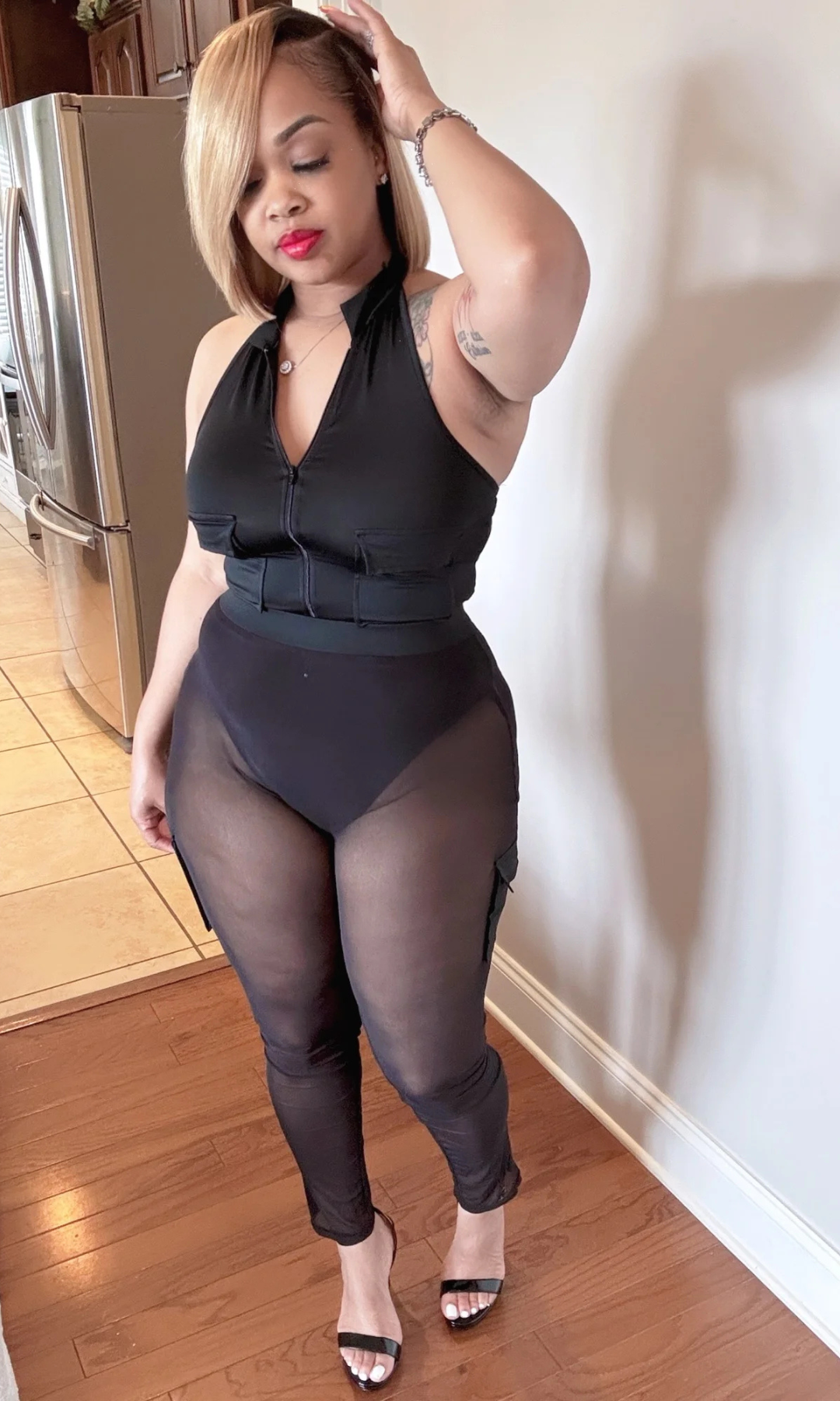 Model wearing Back Outside two-piece set, front view, featuring black zip-front bodysuit and mesh-paneled pants.