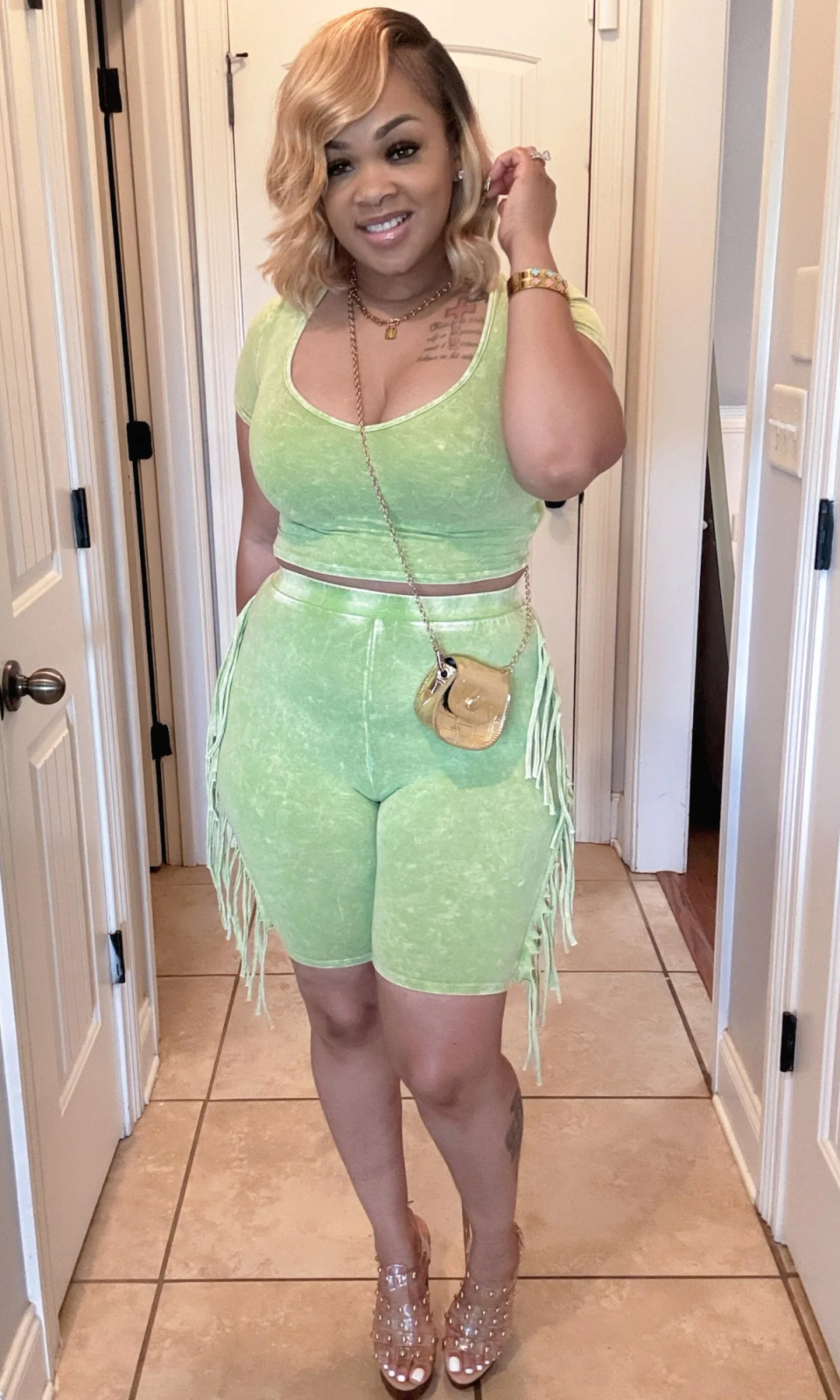 Woman wearing green fringe crop top and biker shorts, smiling, front view.