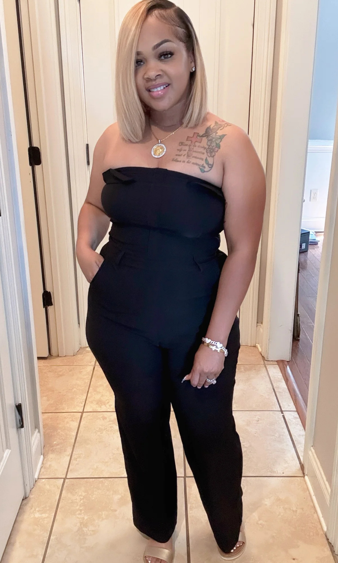 Woman wearing a black strapless Dark Sky jumpsuit standing in a hallway.
