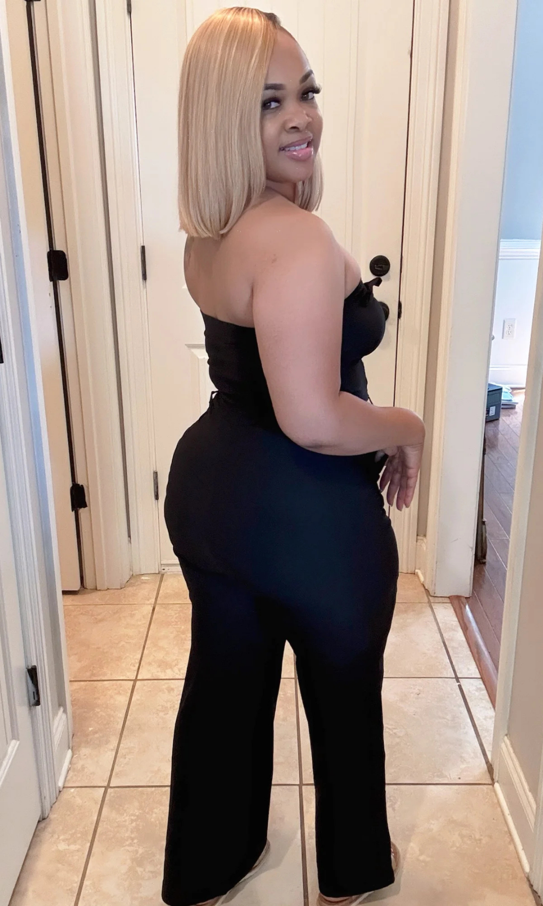 Woman wearing a black strapless Dark Sky jumpsuit in a hallway.