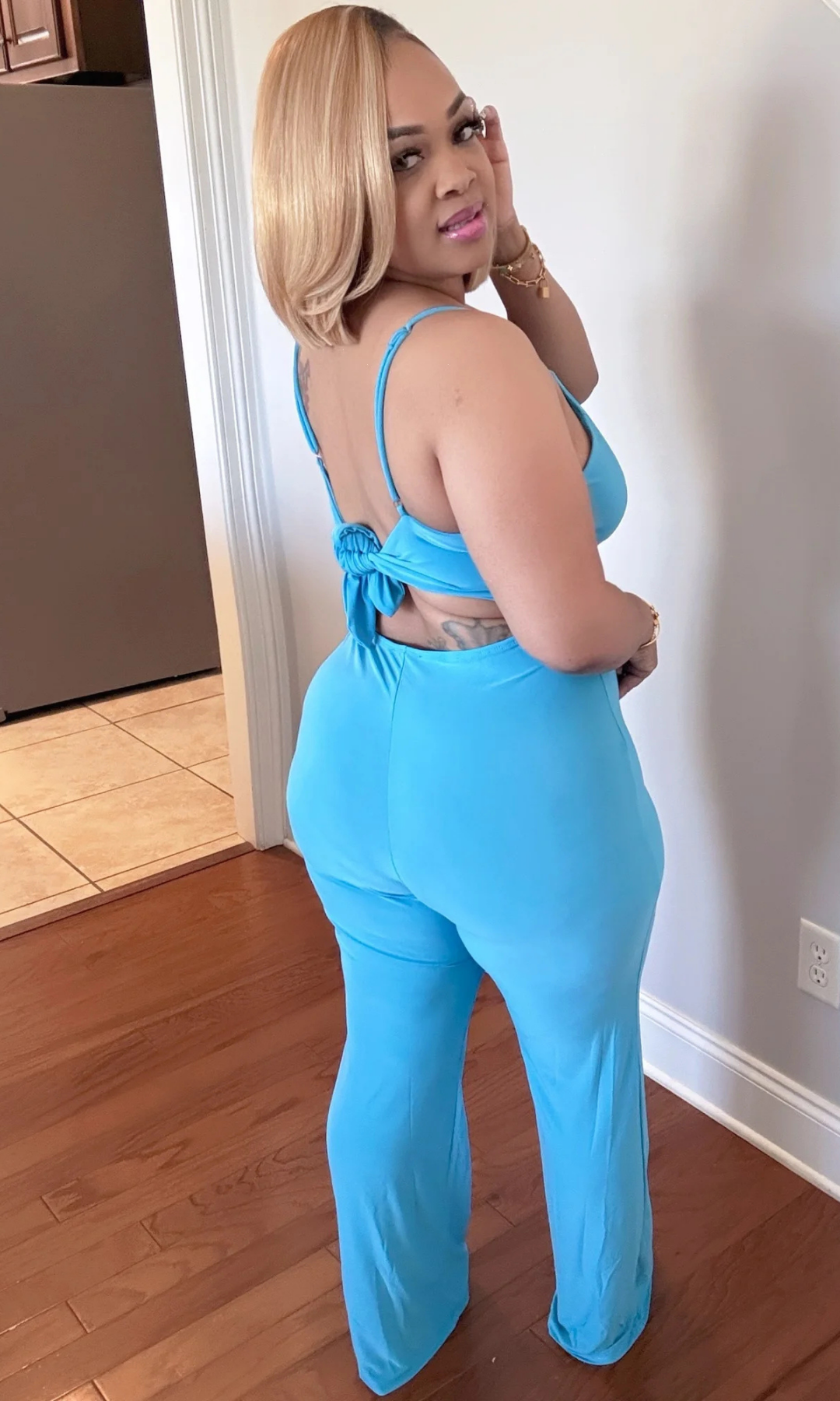 Side pose of model in blue jumpsuit with spaghetti straps and back tie detail.