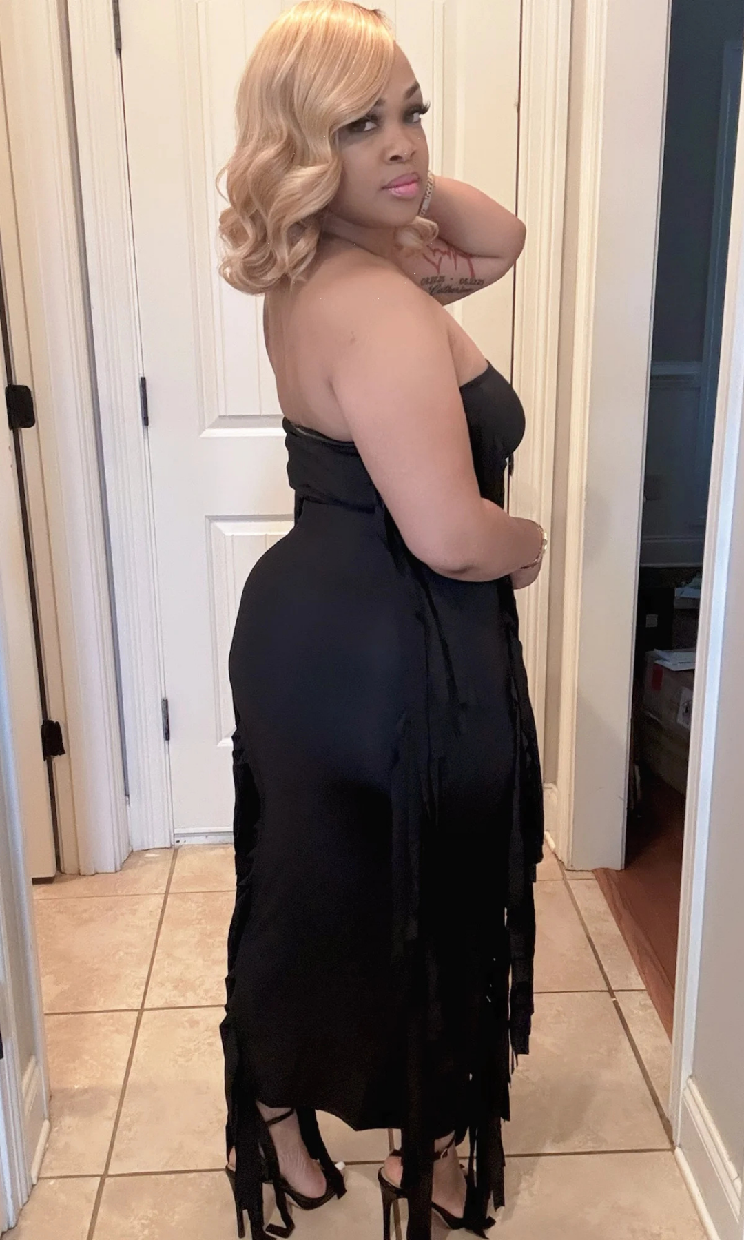Woman wearing a black two-piece skirt set with fringe detailing, back view.