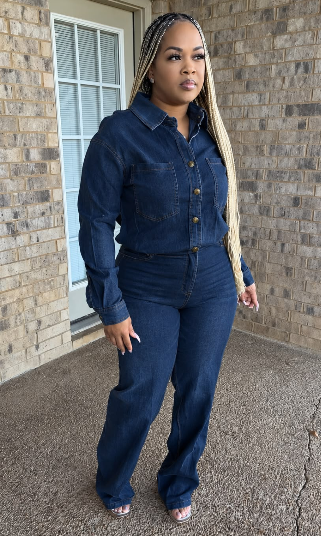 Woman modeling The Blueprint Jumpsuit in dark blue denim, featuring a collared button-down top, long sleeves, two chest pockets, defined waist, and full-length straight-leg pants.