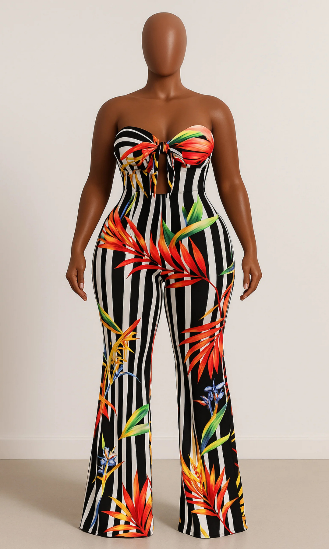 Front view of a strapless tube jumpsuit with black-and-white vertical stripes and large vibrant tropical floral prints in red, yellow, orange, green, and blue, featuring a front tie bust detail and flared legs.
