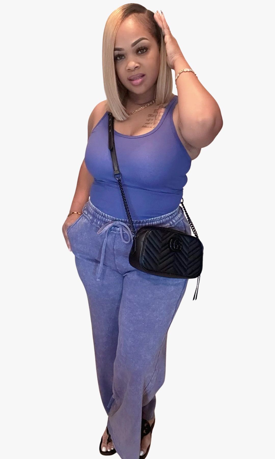 Model in washed blue tank top and wide-leg pants, black crossbody bag, and black slide sandals indoors.
