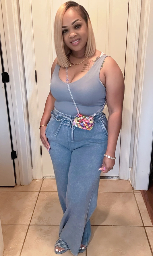 Model in teal tank top and wide-leg pants with colorful beaded crossbody bag indoors.