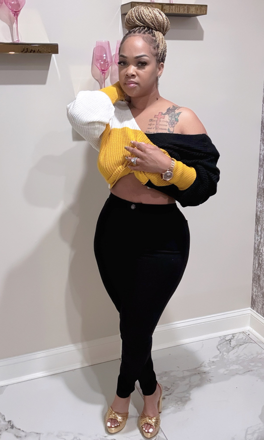 Woman wearing a black and yellow off-shoulder top with black jeans.