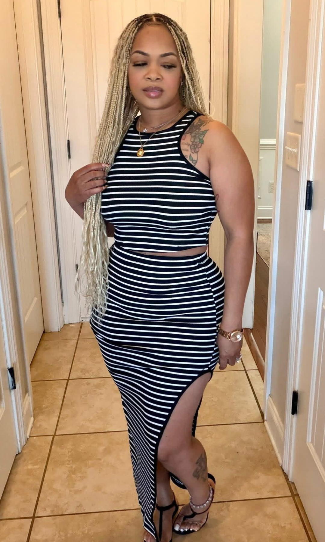 Woman wearing a black and white striped two-piece set with a sleeveless crop top and high-waisted maxi skirt featuring a side slit.