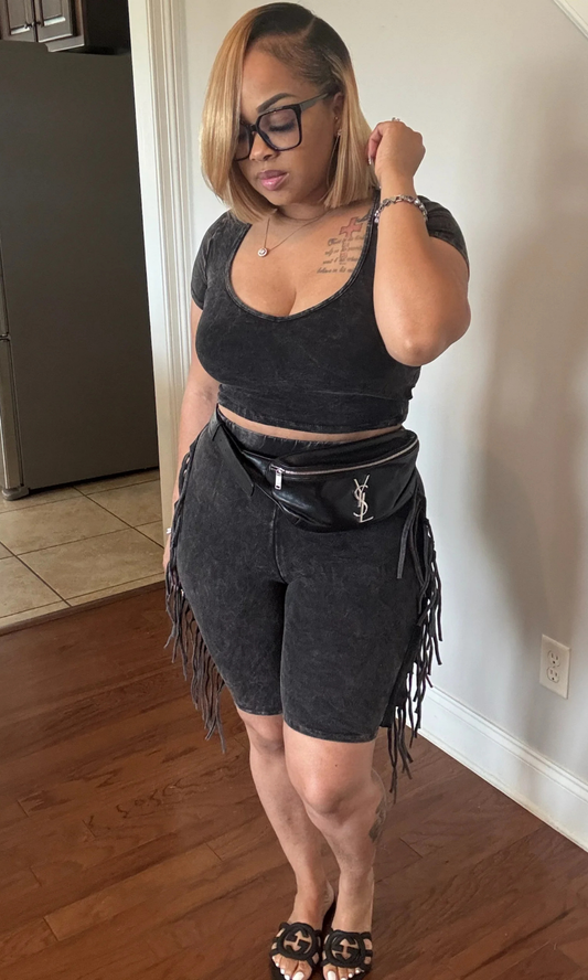Woman wearing black two-piece fringe set, front view, styled with black sandals and belt bag.