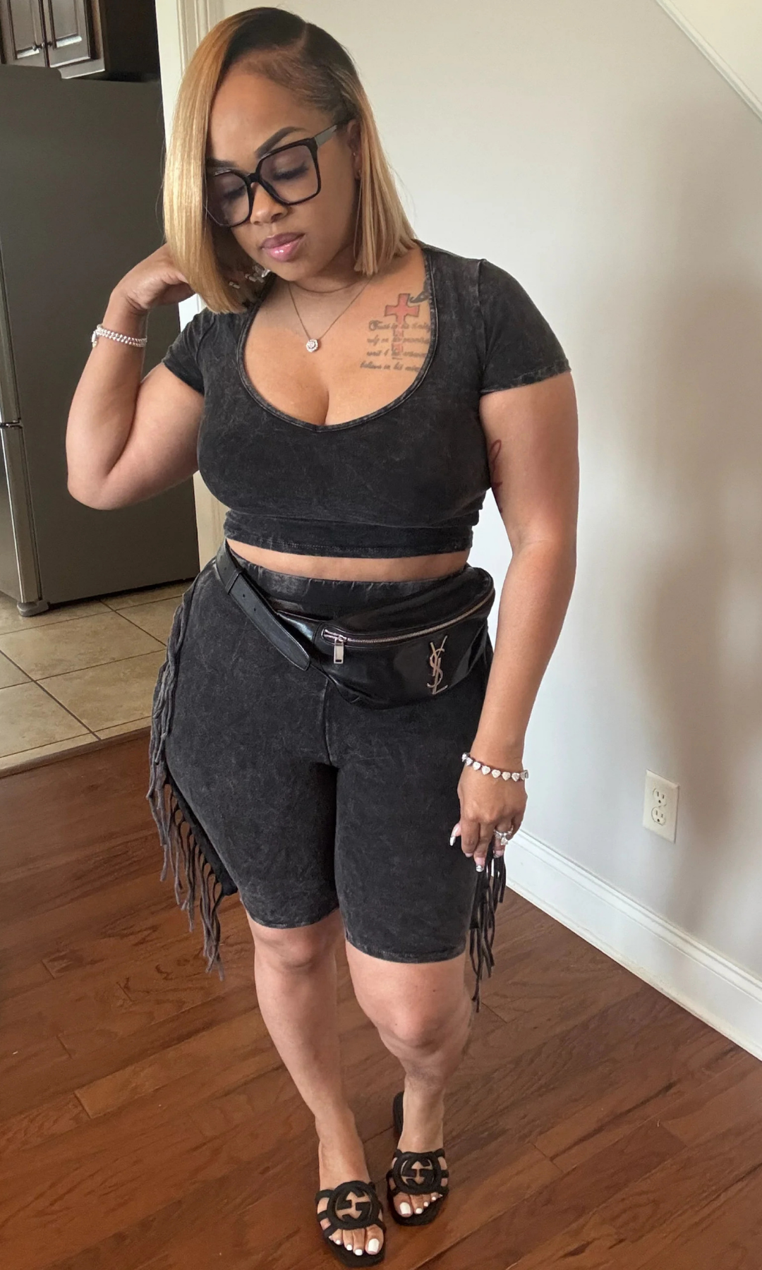 Woman posing in black two-piece fringe set, side view with accessories.