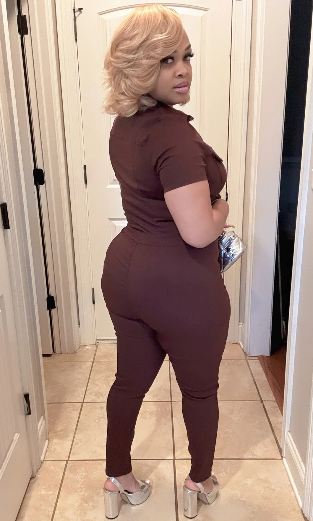 Woman wearing a brown jumpsuit standing in a hallway.