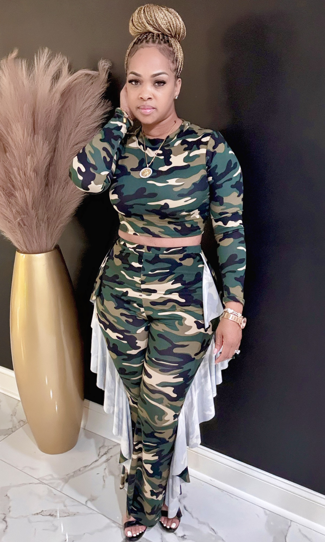 Woman in camouflage outfit standing next to a decorative vase against a dark wall.
