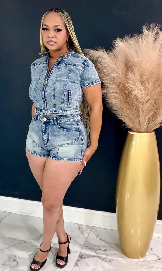 Woman wearing the Denim Hottie two-piece set featuring a cropped zip-front denim jacket and high-waisted acid-wash denim shorts.