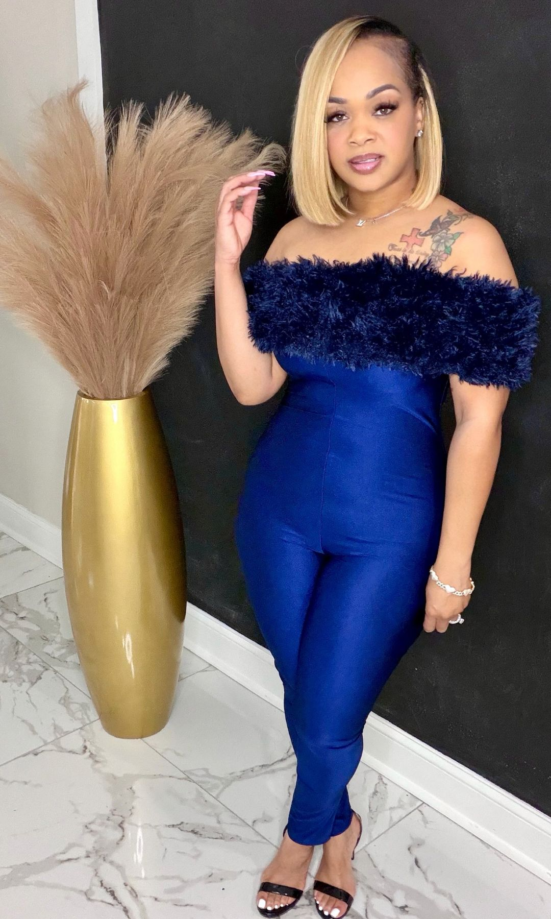Woman wearing navy off-shoulder feather trim jumpsuit with fitted silhouette and stretch fabric, front view.