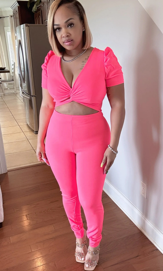 Woman wearing hot pink jumpsuit with twist-front top and cut-out midriff, front view.