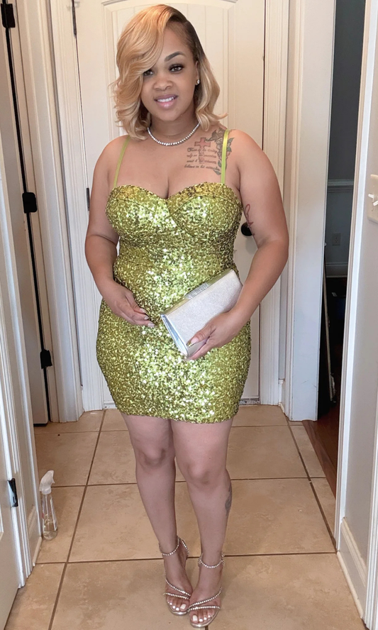 Woman wearing a green sequin dress in a room with white walls and a tiled floor.