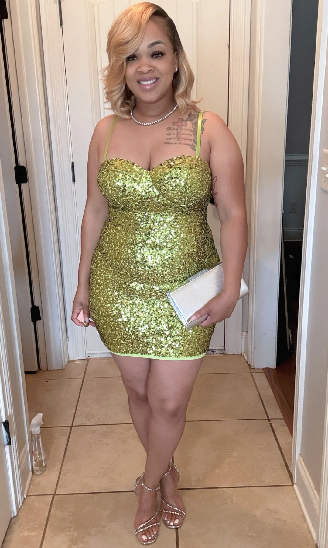 Woman wearing a green sequin dress holding a white clutch indoors.