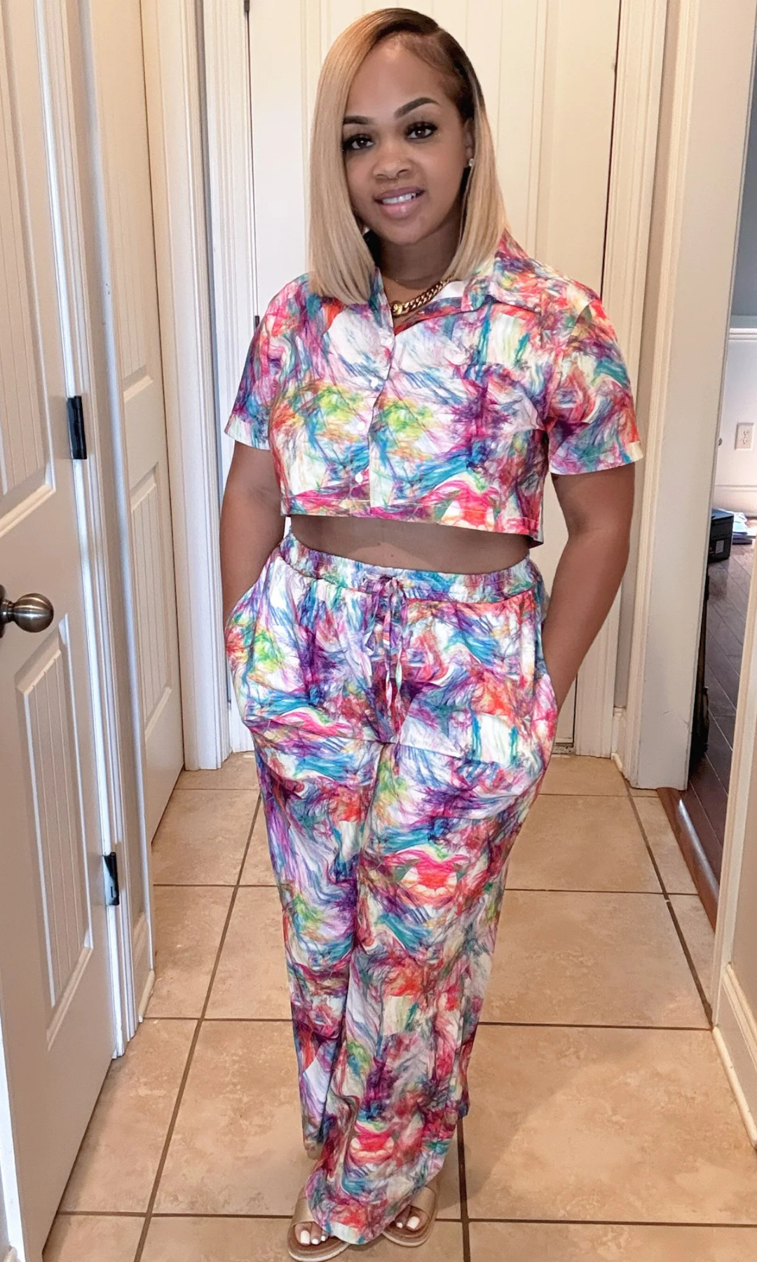 Woman wearing a colorful outfit standing in a room with tiled floor and white walls.