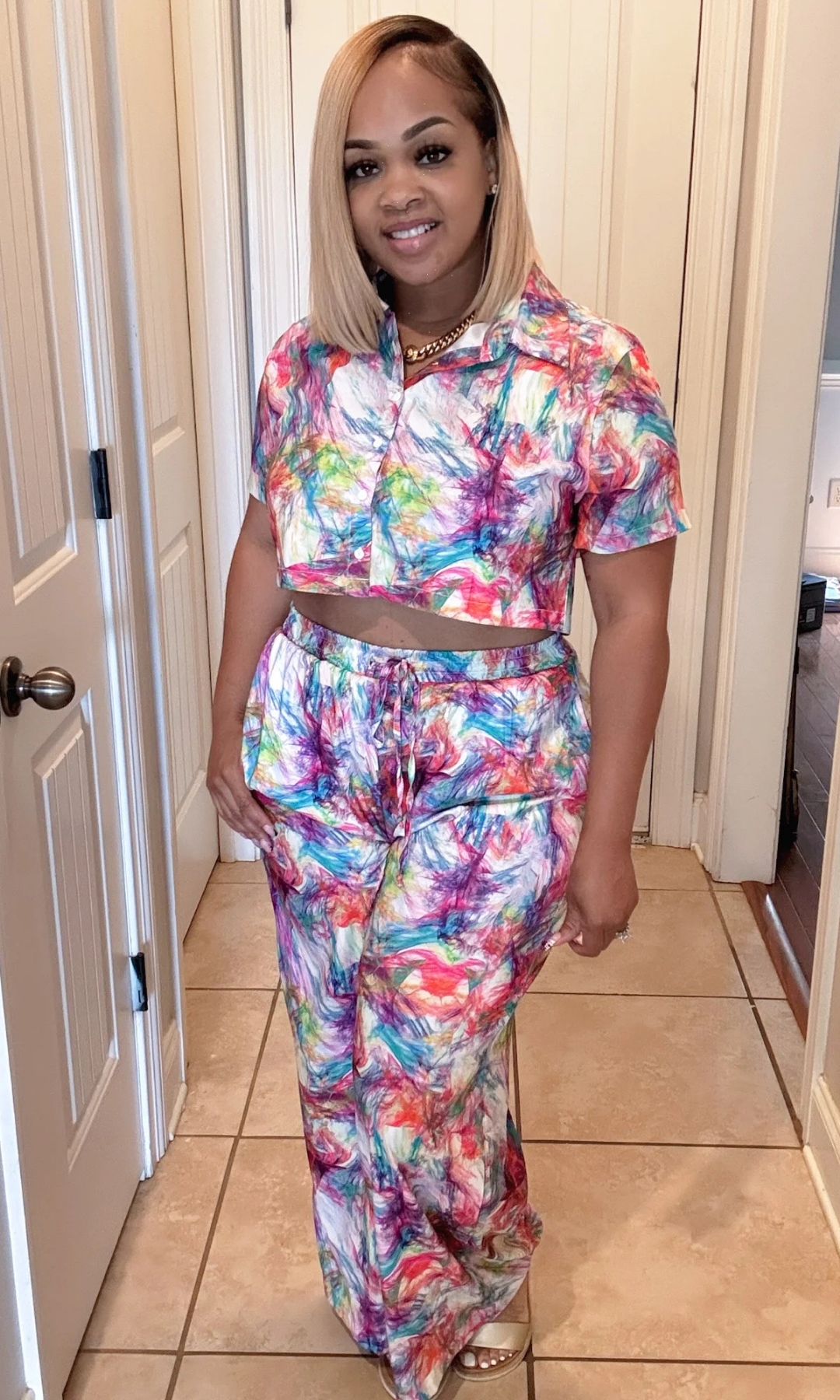 Woman wearing a colorful outfit standing in a room with a door and tiled floor.