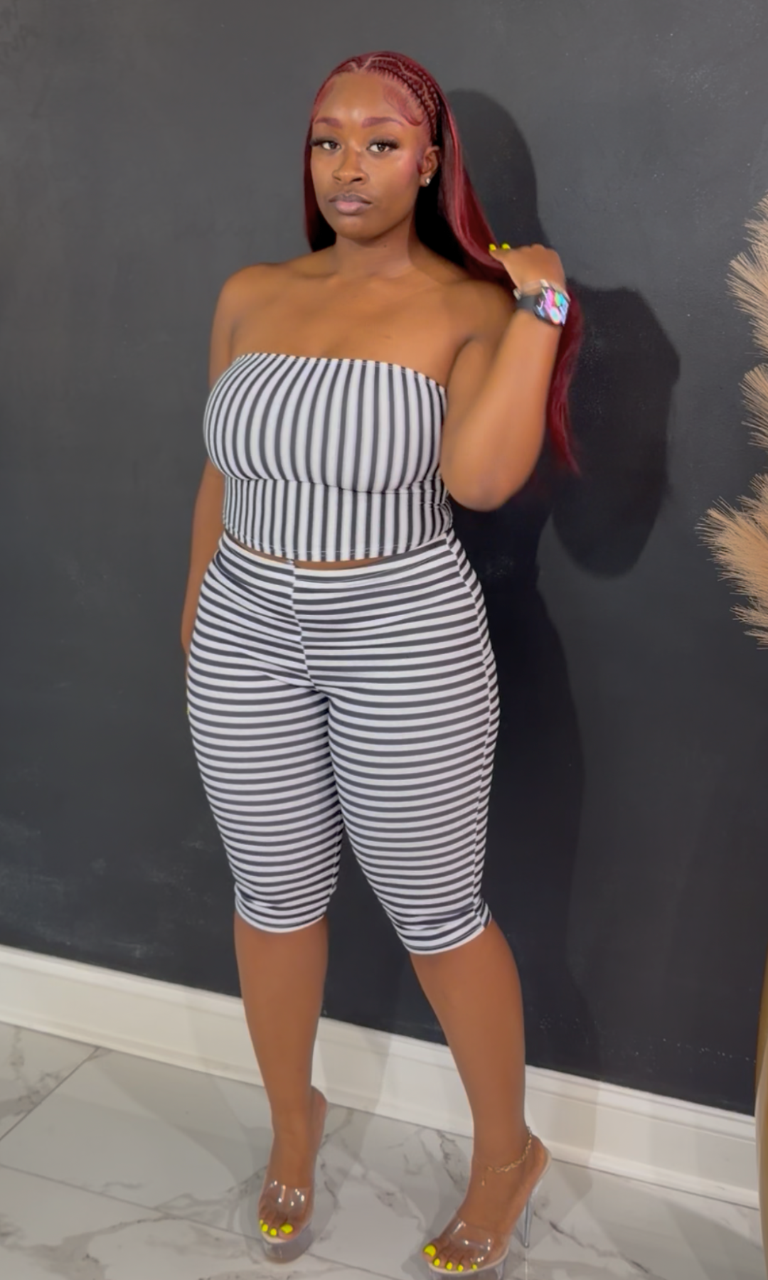 A woman modeling a matching two-piece set consisting of a strapless bandeau crop top and high-waisted striped capri pants, featuring black and white horizontal stripes.