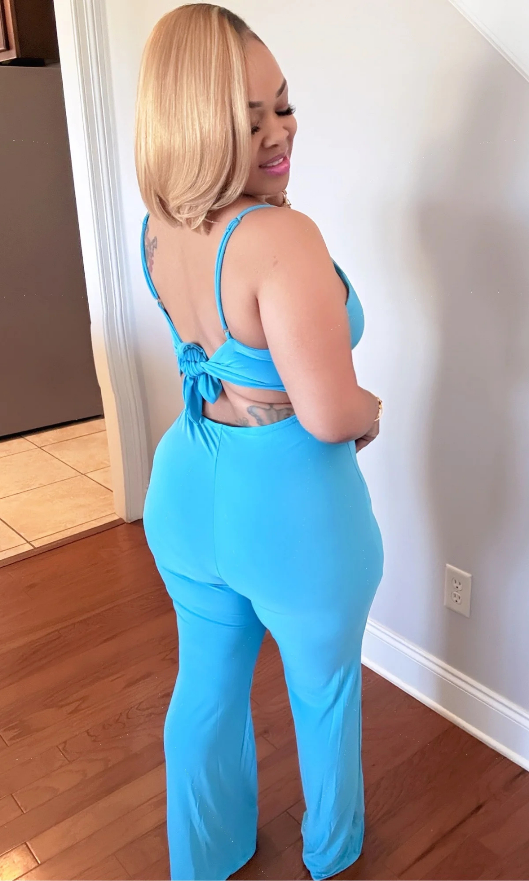 Rear view of model in blue jumpsuit showing open back with knotted tie detail.