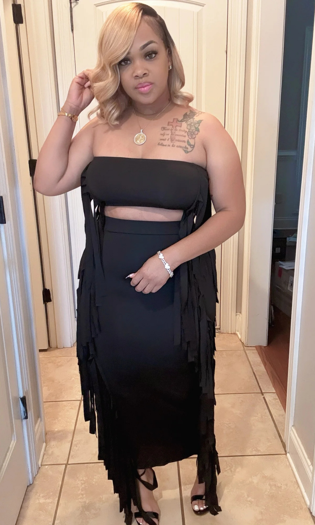 Woman wearing a black two-piece skirt set with fringe detailing, front view.