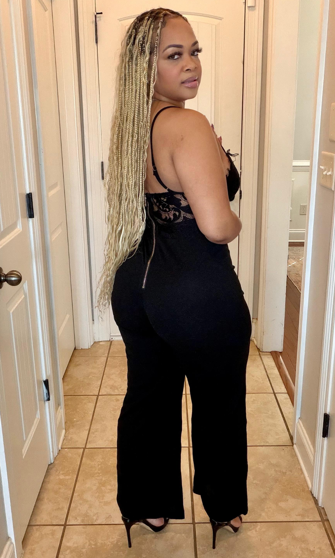 Woman wearing a black jumpsuit with lace detailing in a hallway.