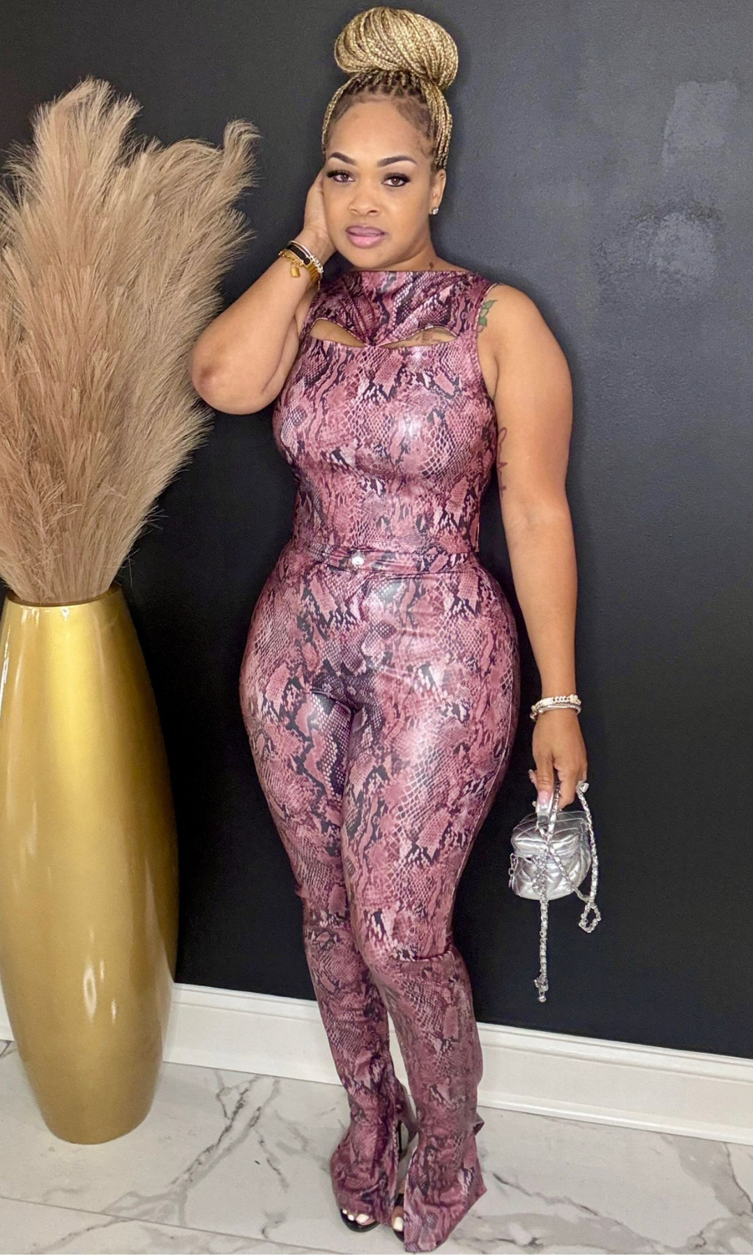 Woman in a pink snake print jumpsuit posing against a black wall with decorative elements.