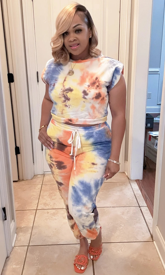Front view of woman wearing the Take It Back Set in vibrant orange, yellow, blue, and brown tie-dye print with padded-shoulder sleeveless top and drawstring joggers.