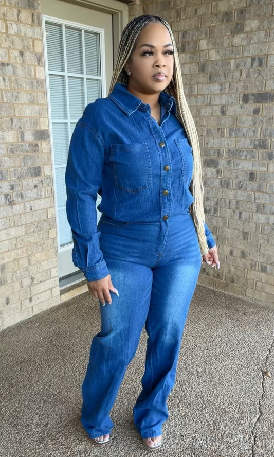 Woman modeling The Blueprint Jumpsuit in medium-light blue denim, featuring a collared button-down top, long sleeves, two chest pockets, defined waist, and full-length straight-leg pants.