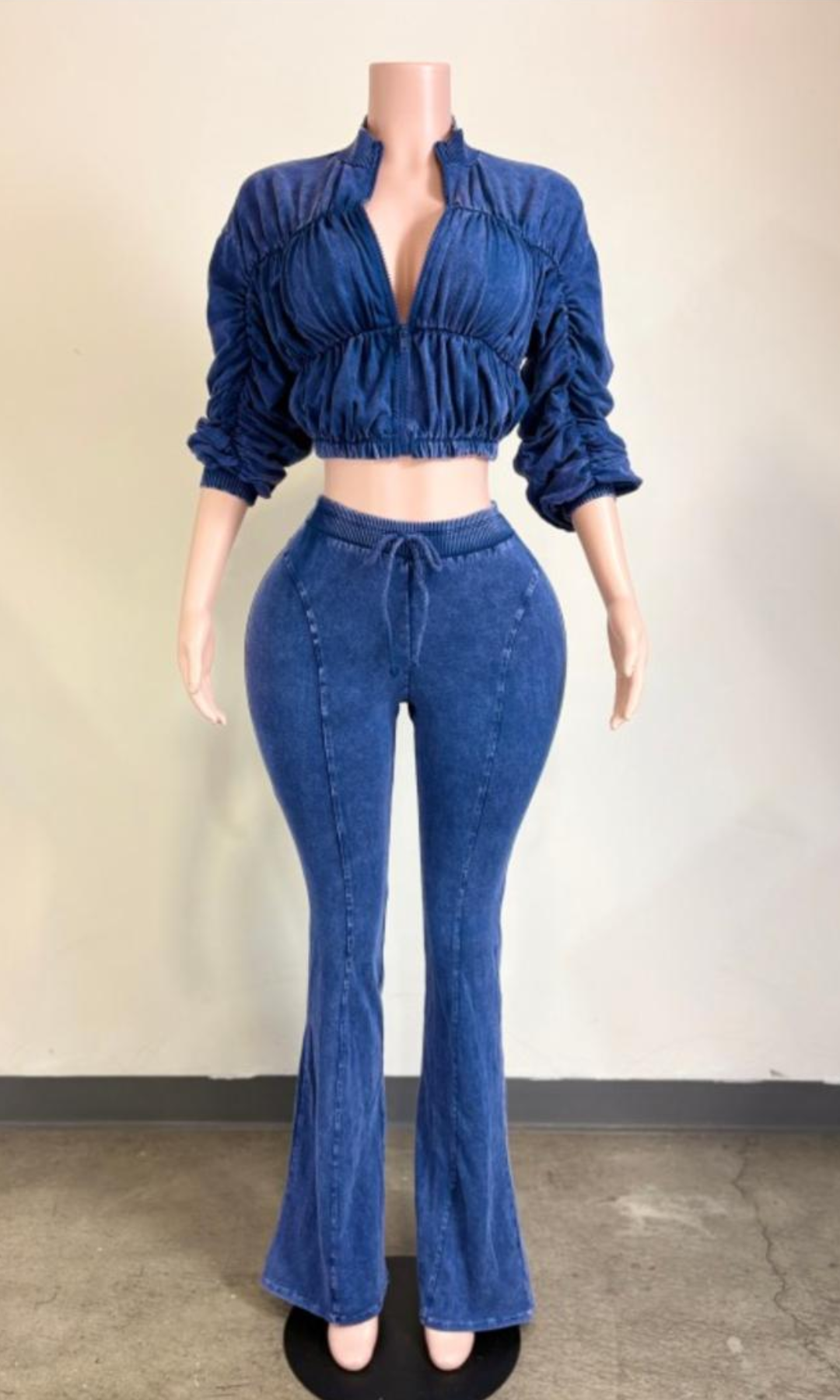 Blue acid-wash two-piece matching set featuring a cropped zip-front jacket with ruched detailing, gathered sleeves, and high-waisted drawstring flared pants displayed on a mannequin.
