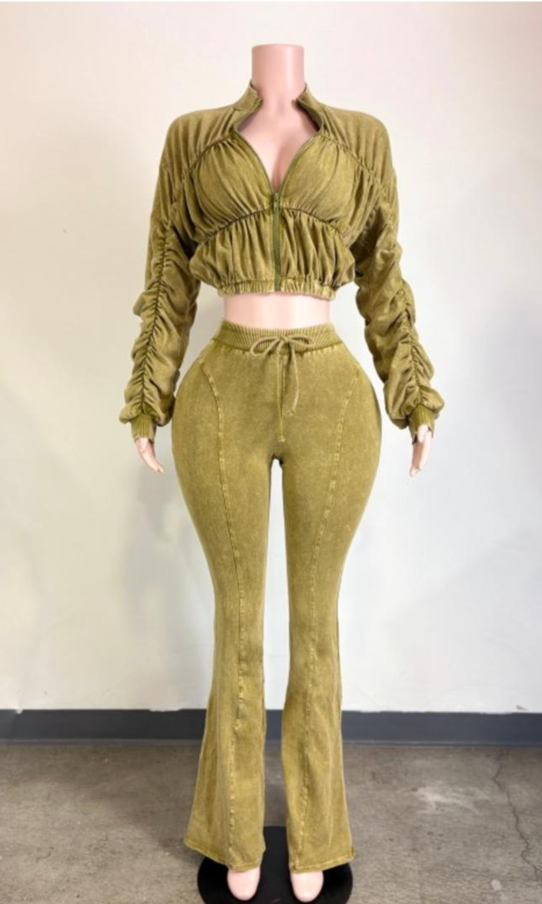 Olive-green acid-wash two-piece matching set featuring a cropped zip-front jacket with ruched detailing, gathered long sleeves, and high-waisted drawstring flared pants displayed on a mannequin.