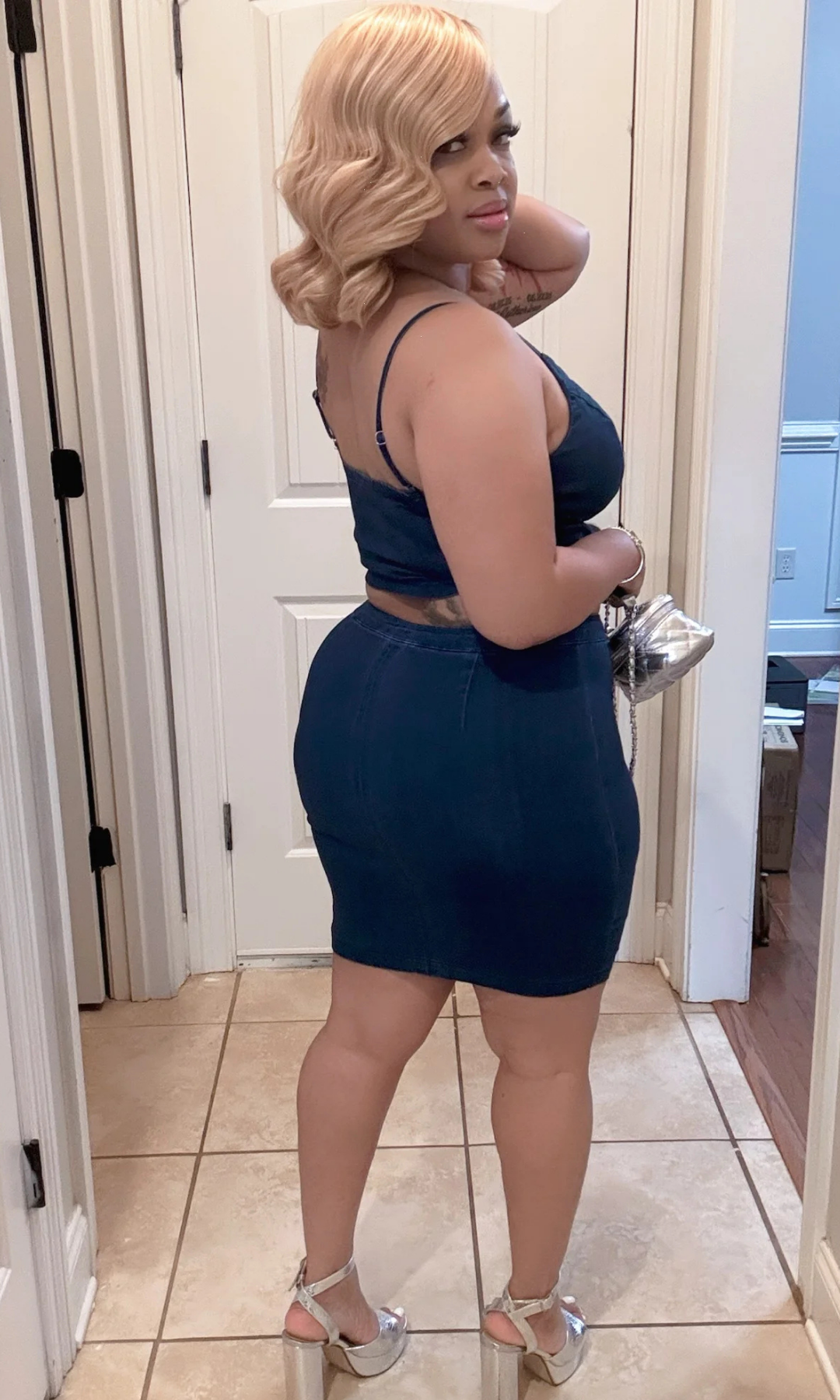 Back view of model in the Unzip Me Jean Set, showcasing the body-hugging fit of the dark wash denim skirt and adjustable spaghetti straps on the matching crop top, paired with platform silver heels.