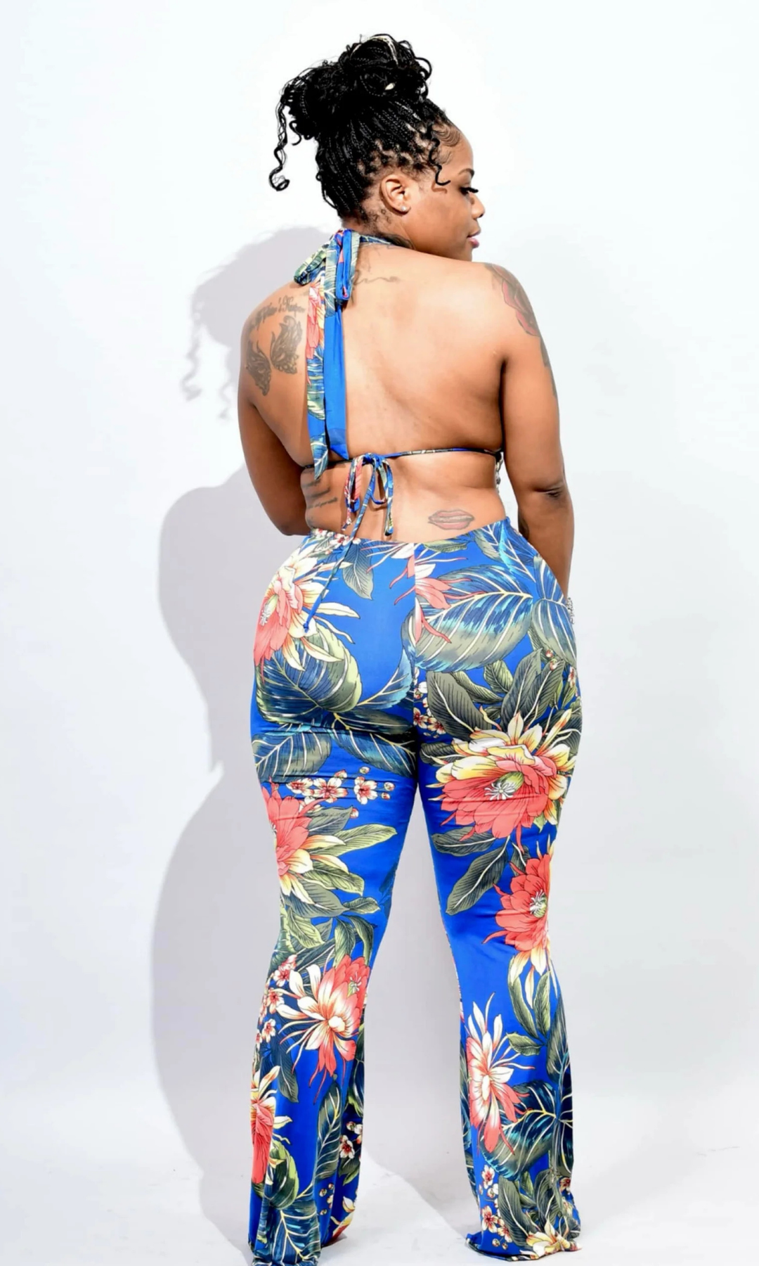 Vacation Party Jumpsuit Back View – Woman wearing royal blue tropical floral jumpsuit with open-back halter design, wide-leg pants, and vibrant coral and green leaf print.
