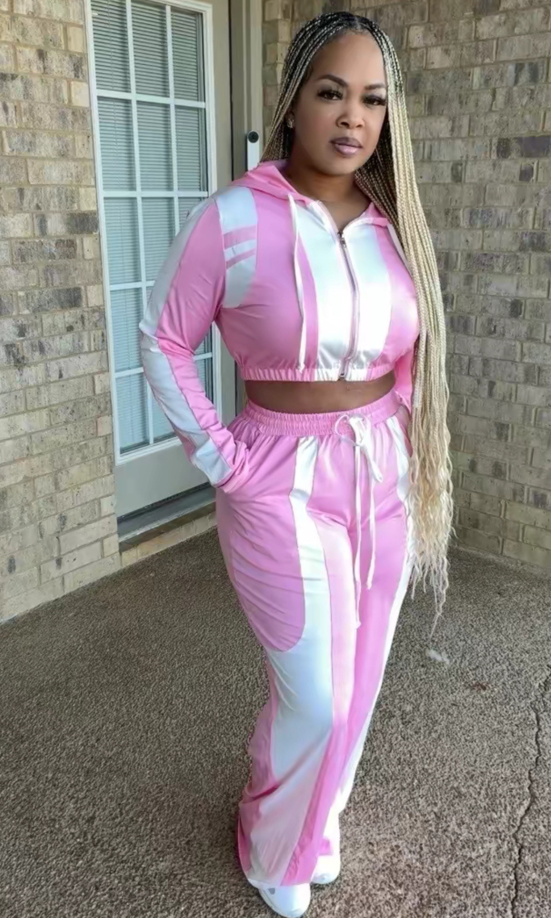 A woman modeling the Bubblegum Tracksuit featuring a pink and white cropped zip-up hoodie with drawstrings and matching high-waisted wide-leg pants.