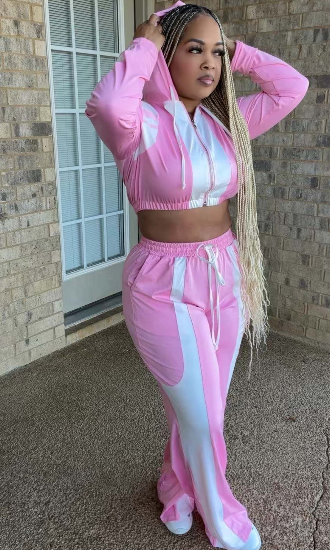 Woman modeling the Bubblegum Tracksuit featuring a pink and white cropped zip-up hoodie with drawstrings and matching high-waisted wide-leg pants.