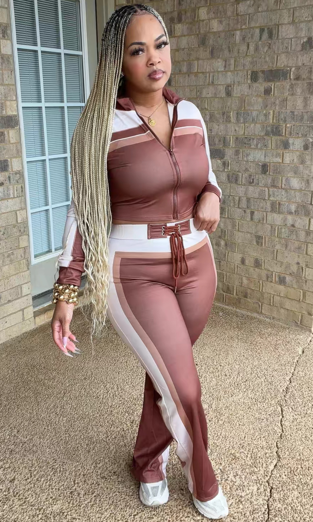 Woman modeling the Cashmere Set Brown featuring a chocolate brown, ivory, and nude cropped zip-up jacket with matching high-waisted wide-leg pants and lace-up waistband.