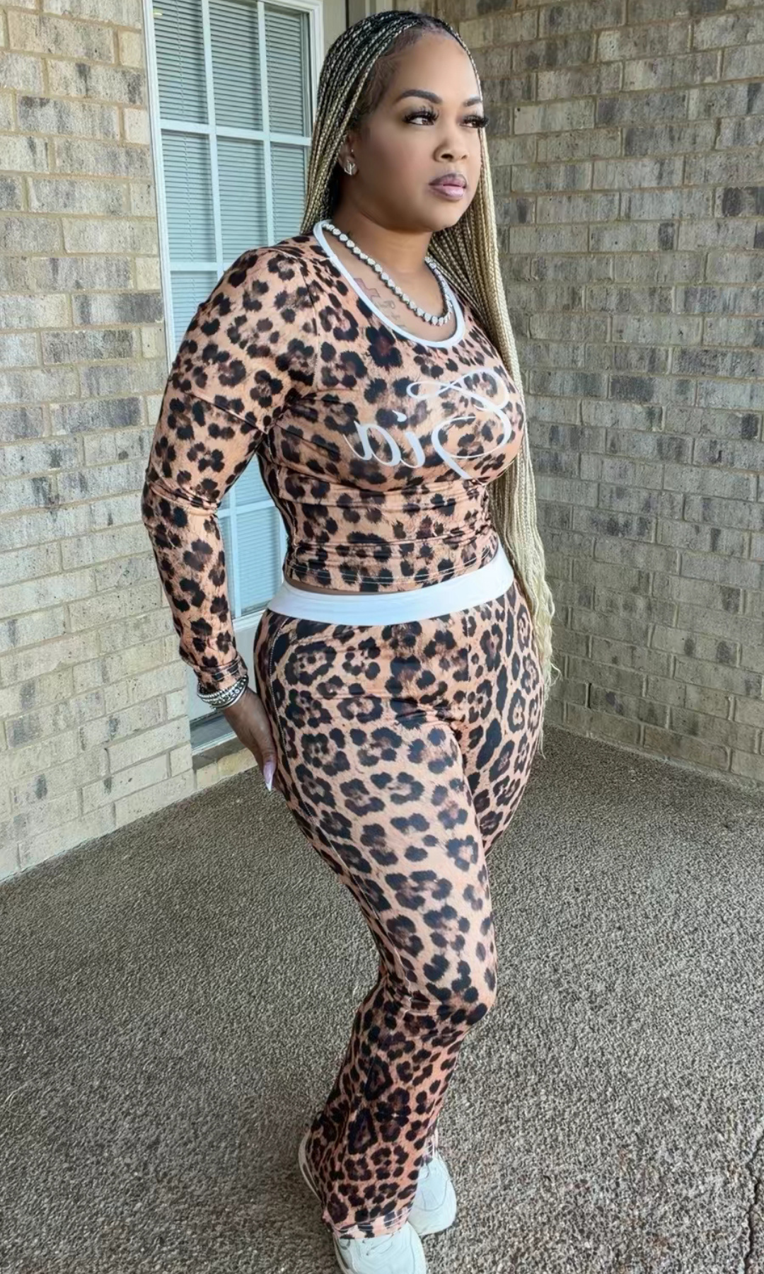 Woman modeling the Cheetah Inspired Gia two-piece set featuring a brown and black leopard-print long-sleeve top with white script detailing and matching high-waisted pants.
