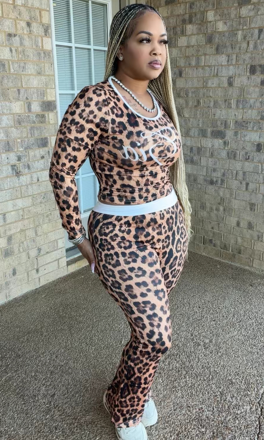 Woman modeling the Cheetah Inspired Gia two-piece set featuring a brown and black leopard-print long-sleeve top with white script detailing and matching high-waisted pants.