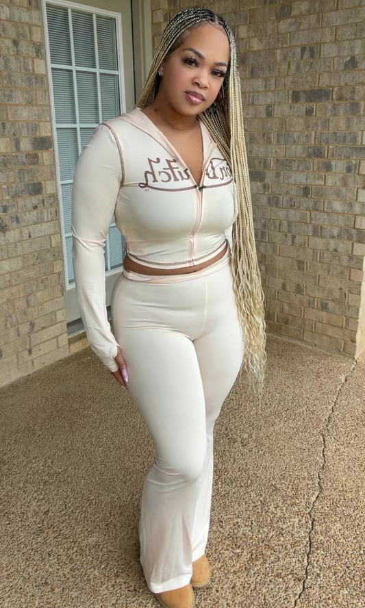 Woman modeling the Cream VD Two-Piece Set featuring a cream long-sleeve cropped zip-up hoodie with brown graphic lettering and matching high-waisted flared pants.