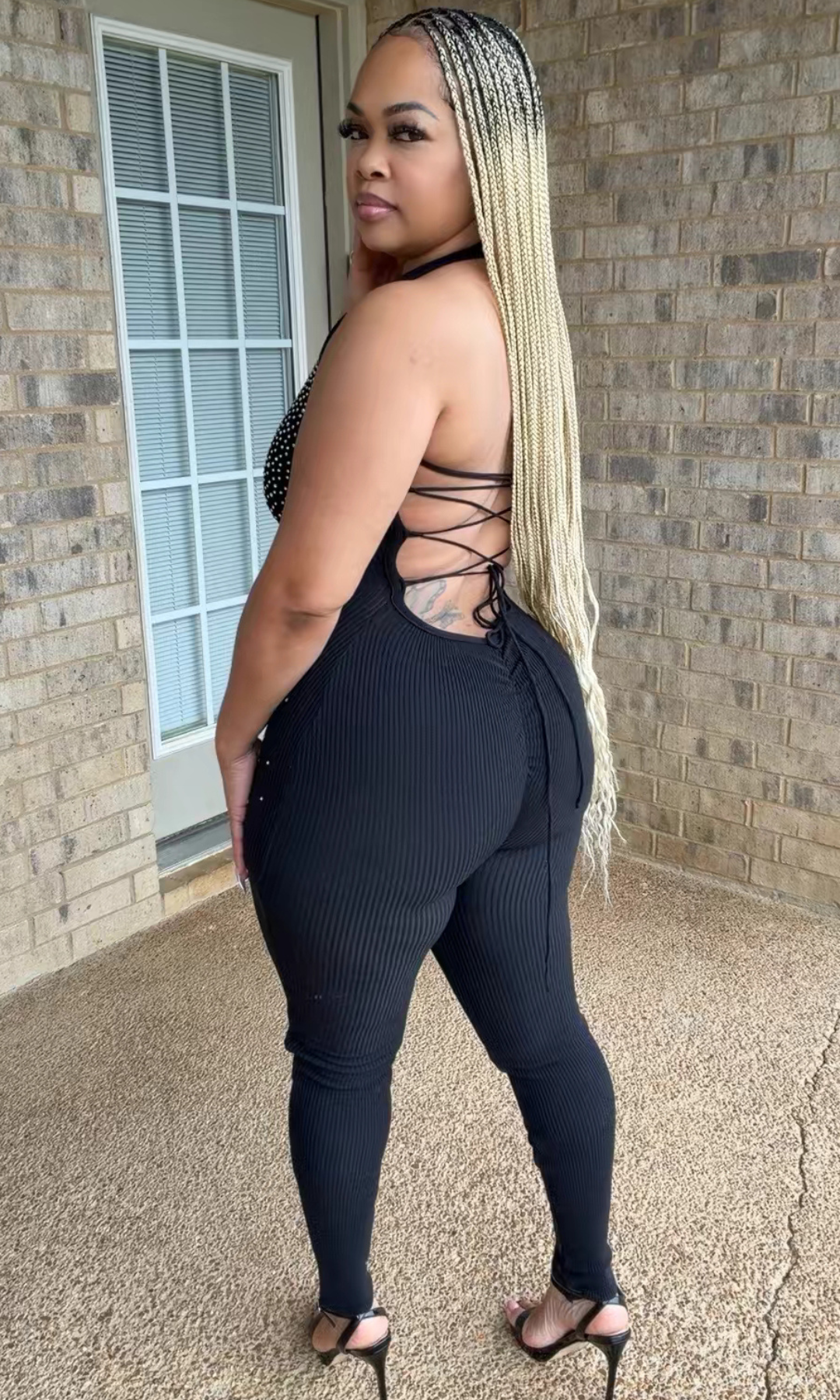 Side and back view of the Diamond Doll Jumpsuit featuring an open-back design with crisscross lace-up detailing, fitted ribbed fabric, and a sleek black silhouette.