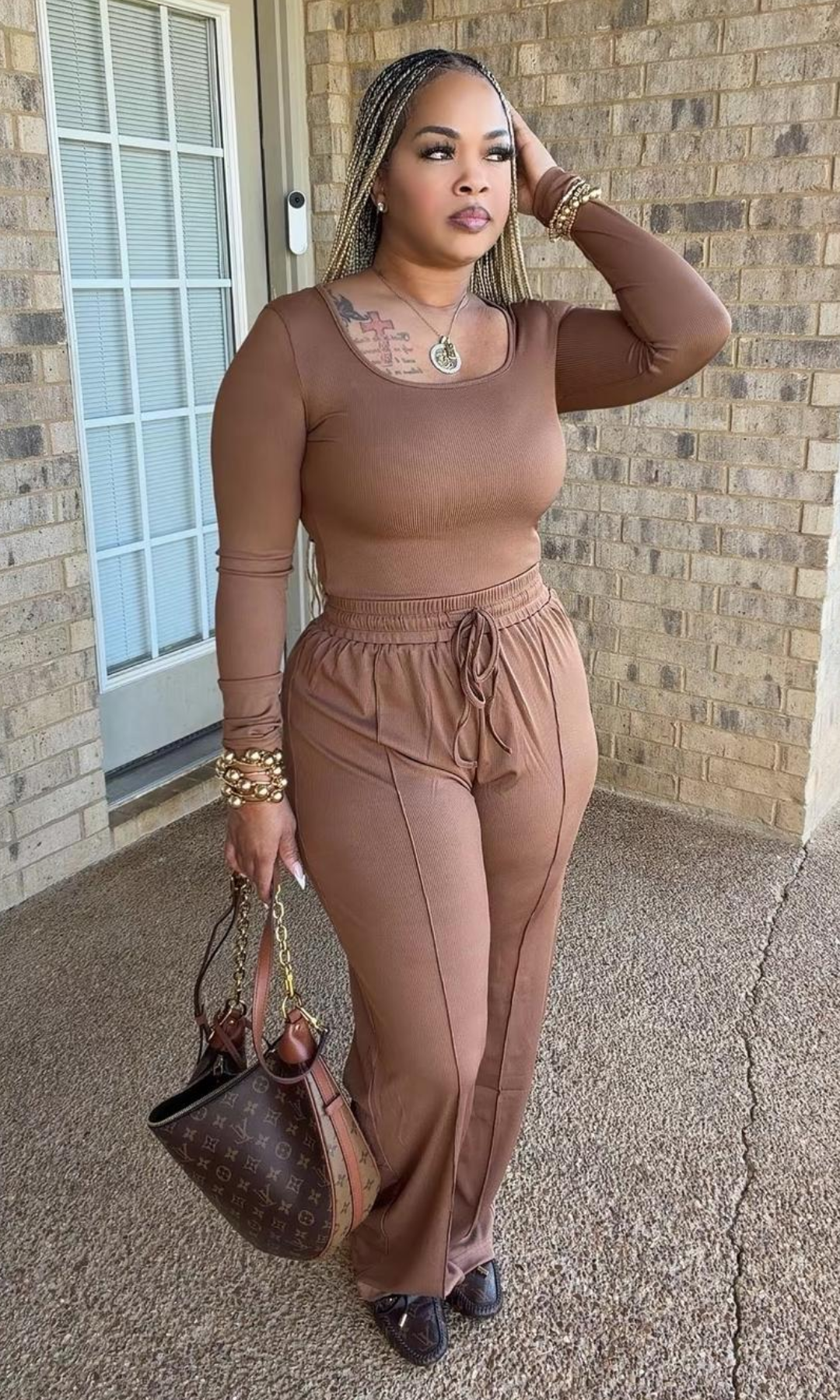 Model wearing the Honey Graham Bodysuit Set in warm brown, featuring a fitted long-sleeve scoop-neck bodysuit and matching high-waisted drawstring wide-leg pants, styled with gold accessories and a brown handbag.