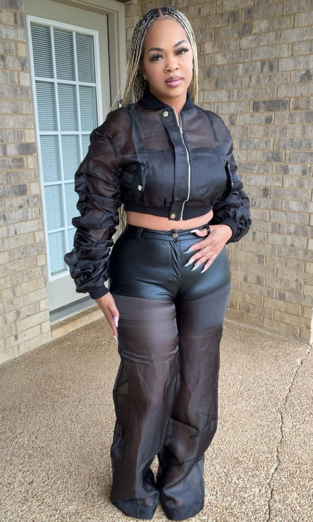 Woman modeling the Now You See Me Set featuring a black cropped sheer bomber jacket with ruched sleeves and coordinating high-waisted pants with leather-look and sheer wide-leg detailing.