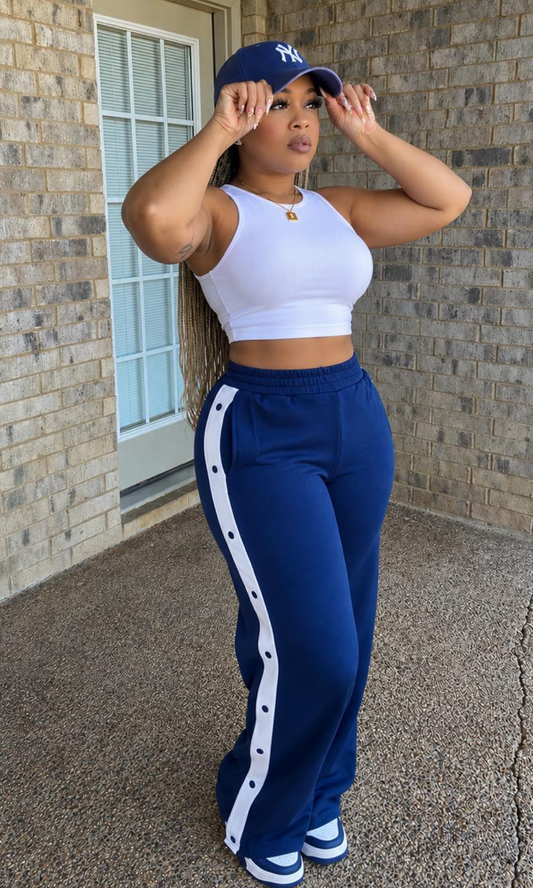Model wearing Oh Snap Track Pants Blue featuring navy blue wide-leg pants with an elastic waistband and white snap-button side panels.