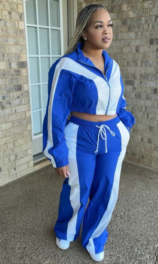 Woman modeling the Sonic Stripe Tracksuit in royal blue and white, featuring a cropped zip-front jacket with bold stripe detailing and matching high-waisted wide-leg track pants.