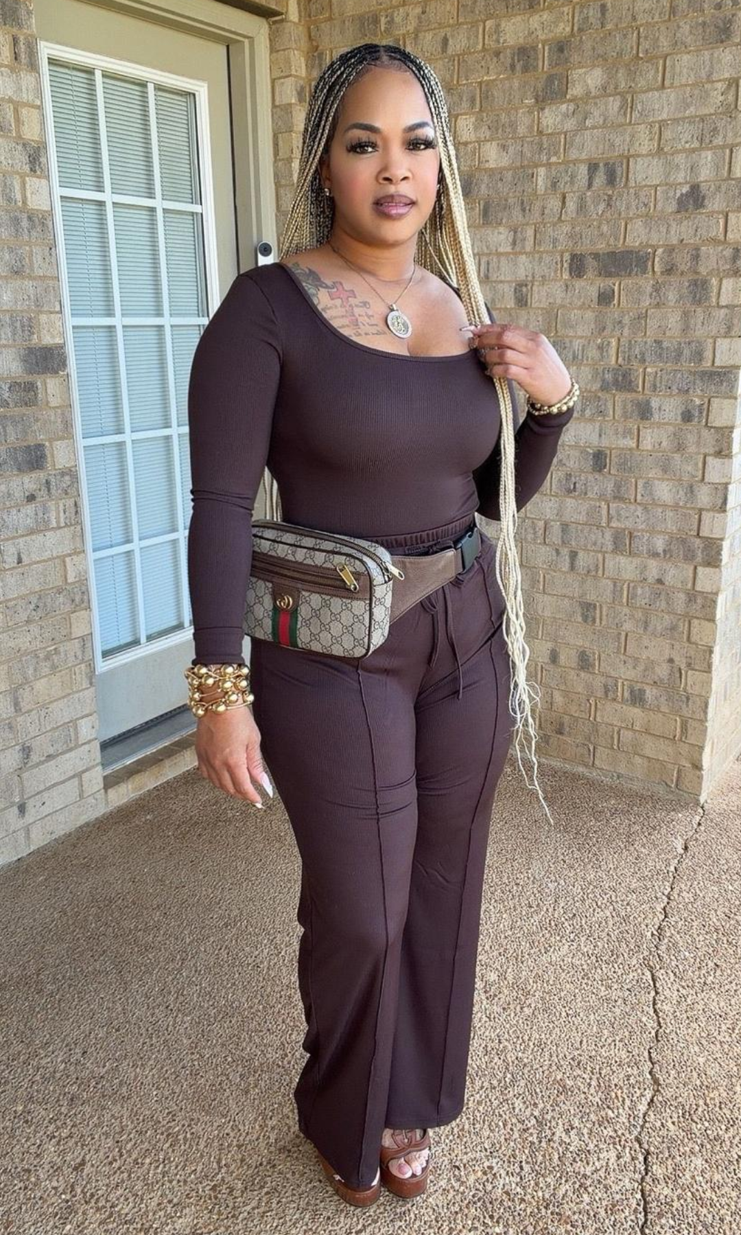 Model wearing the Sweet Cocoa Bodysuit Set in deep chocolate brown, featuring a fitted long-sleeve scoop-neck bodysuit and matching high-waisted drawstring wide-leg pants, styled with a designer-inspired waist bag and gold accessories.
