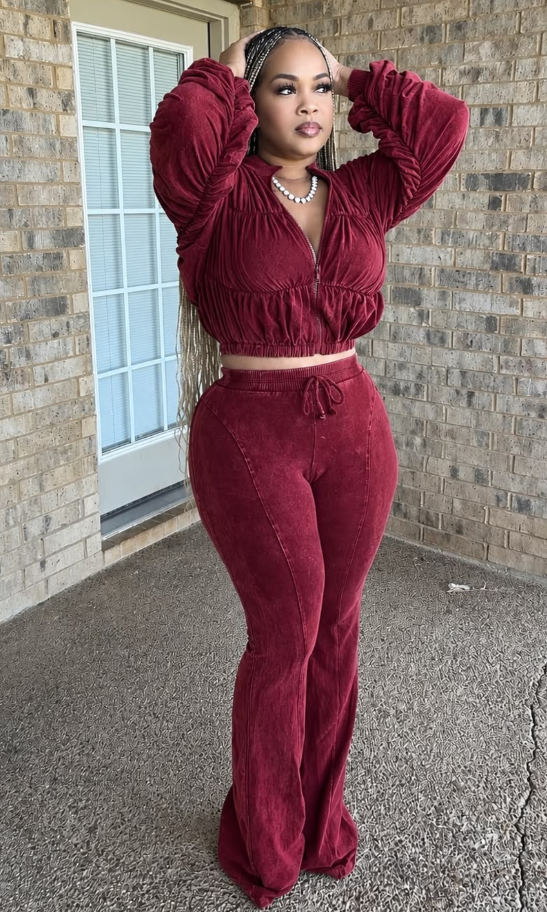 The model is wearing the Weekend Ruched Set Red showing ruched detailing across the cropped jacket, gathered sleeves, elasticized hem, and matching high-waisted flared pants.